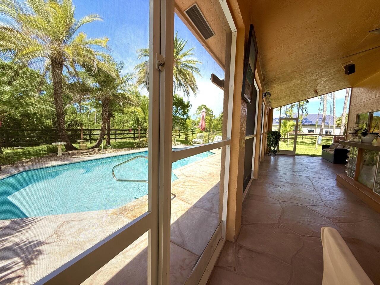 A covered patio with stone flooring overlooks a swimming pool and a fenced backyard — 14765 Northlake Boulevard, FL 33412, FL