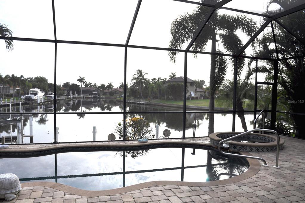 A screened-in pool and hot tub overlook a canal with boats and palm trees — 3293 TRIPOLI BOULEVARD, PUNTA GORDA, FL
