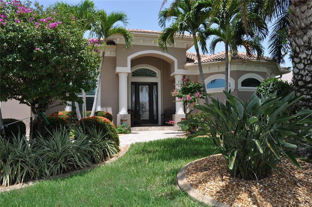 The exterior of a tan house features a covered entryway with columns and palm trees — 3293 TRIPOLI BOULEVARD, PUNTA GORDA, FL