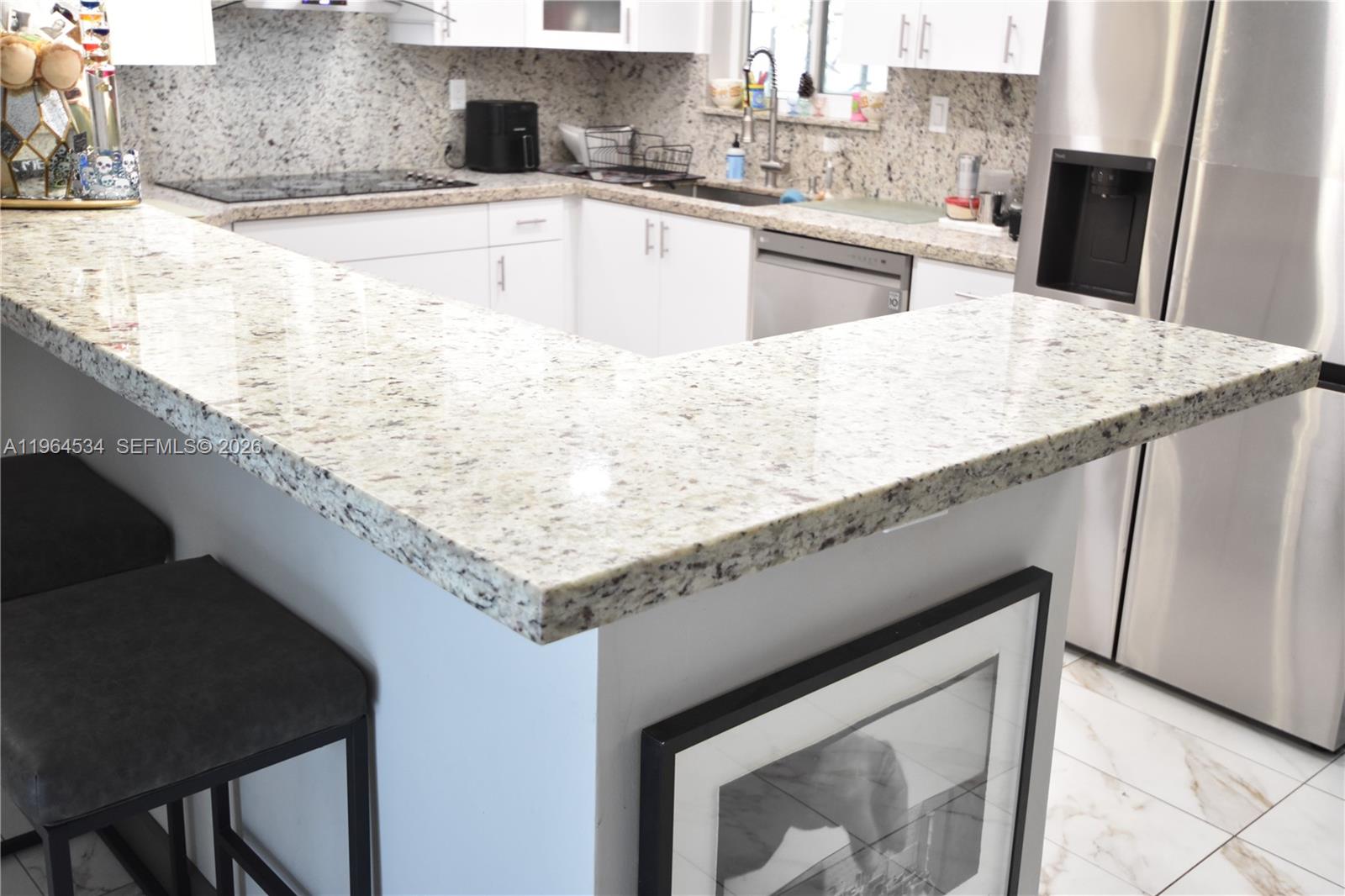 A kitchen features white cabinets, granite countertops, and a breakfast bar with stools — 630 N 66th Ave, Hollywood FL 33024, HOLLYWOOD, FL