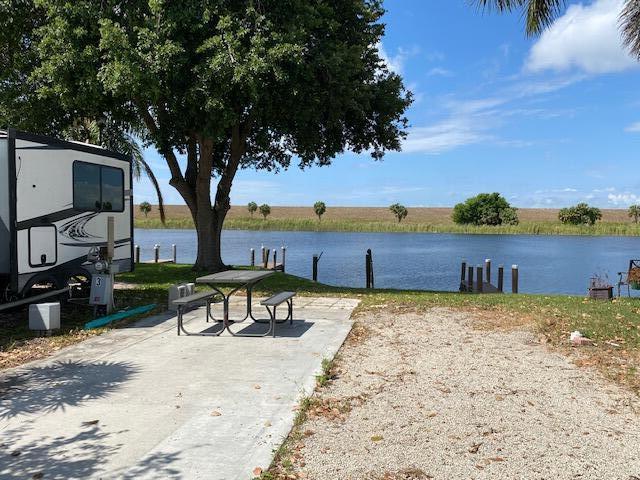 A recreational vehicle is parked on a concrete pad next to a picnic table by water — 8680 Us Highway 441, Okeechobee FL 34974, OKEECHOBEE, FL