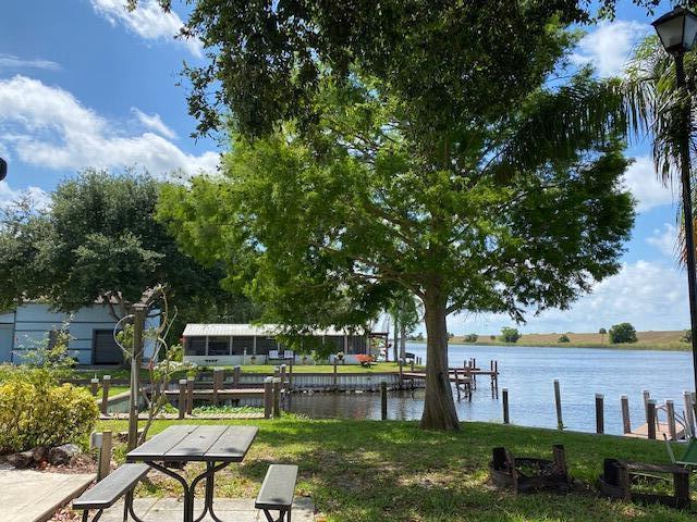 A picnic table sits on a grassy lawn overlooking a river with a wooden dock — 8680 Us Highway 441, Okeechobee FL 34974, OKEECHOBEE, FL