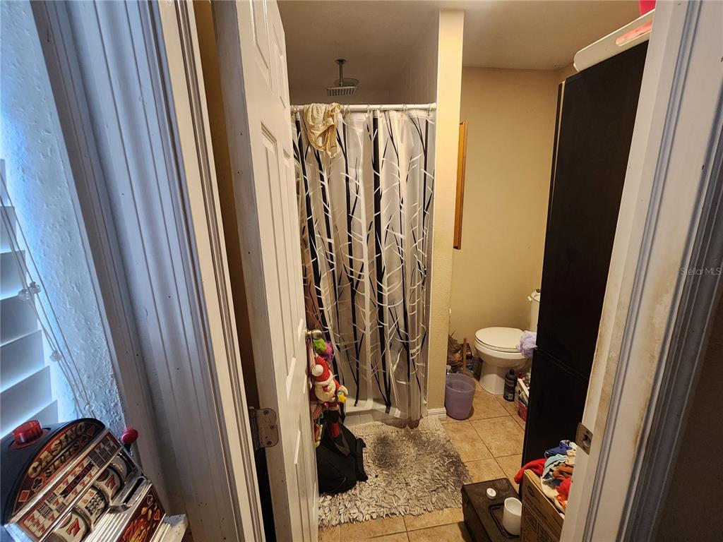 A bathroom features a shower with a patterned curtain, a toilet, and tiled flooring — 1710 MINNIE STREET, COCOA, FL