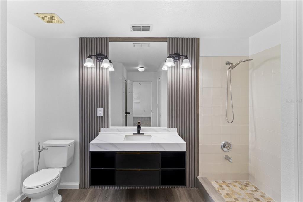 A bathroom features a modern vanity with a marble countertop, vertical wood paneling, and shower — 1601 PERDIDO COURT, KISSIMMEE, FL