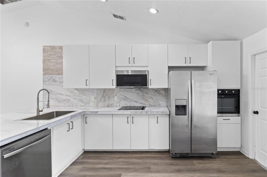 A modern kitchen features white cabinets, stainless steel appliances, and marble-patterned countertops and backsplash — 1601 PERDIDO COURT, KISSIMMEE, FL