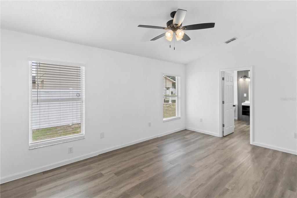 A bedroom with white walls, wood-look flooring, a ceiling fan, and an attached bathroom — 1601 PERDIDO COURT, KISSIMMEE, FL