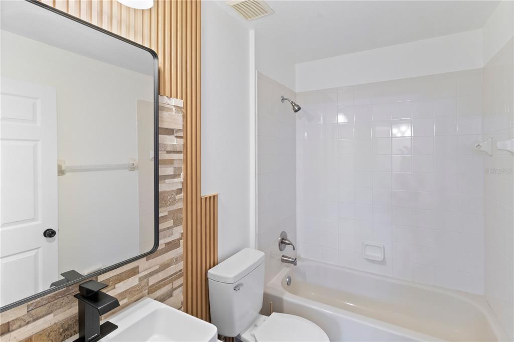 A bathroom features a white bathtub, a toilet, and a vanity with a modern mirror — 1601 PERDIDO COURT, KISSIMMEE, FL