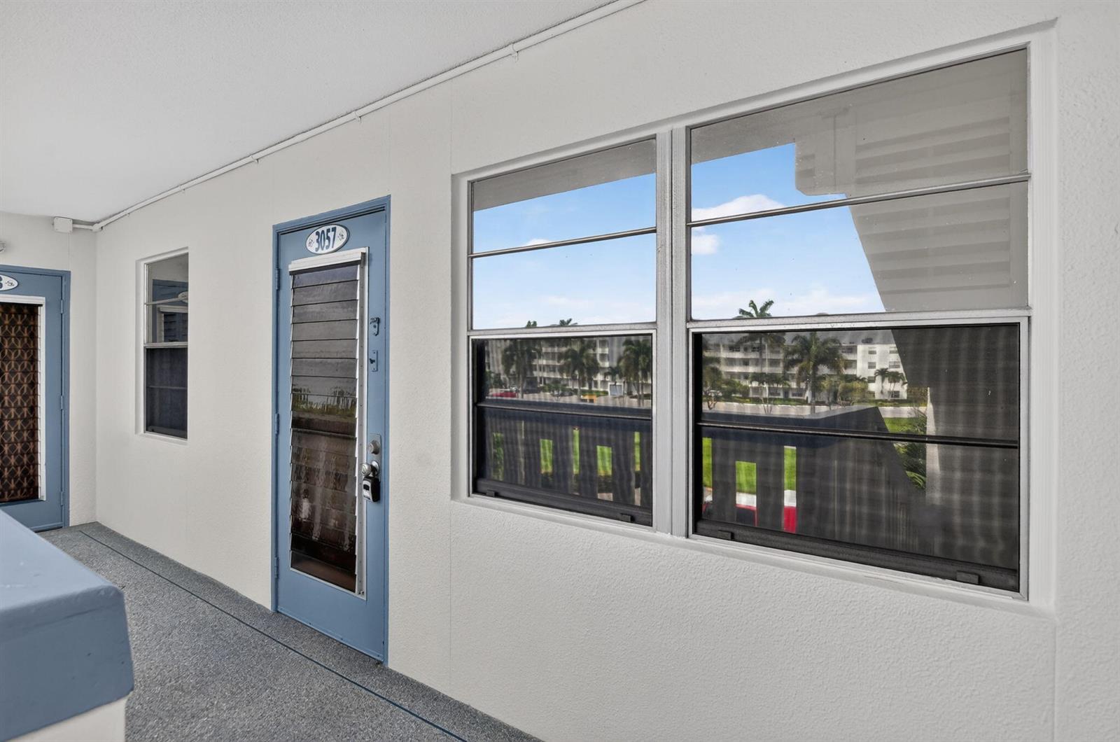 An exterior view of a building hallway featuring a blue door numbered 3057 — 3057 Yarmouth C, Boca Raton FL 33434, BOCA RATON, FL