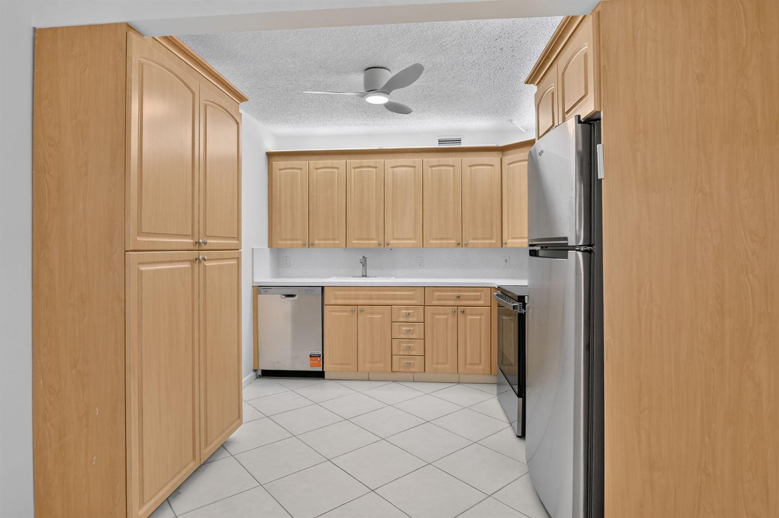 A kitchen features light wood cabinets, stainless steel appliances, white countertops, and tiled flooring — 3057 Yarmouth C, Boca Raton FL 33434, BOCA RATON, FL
