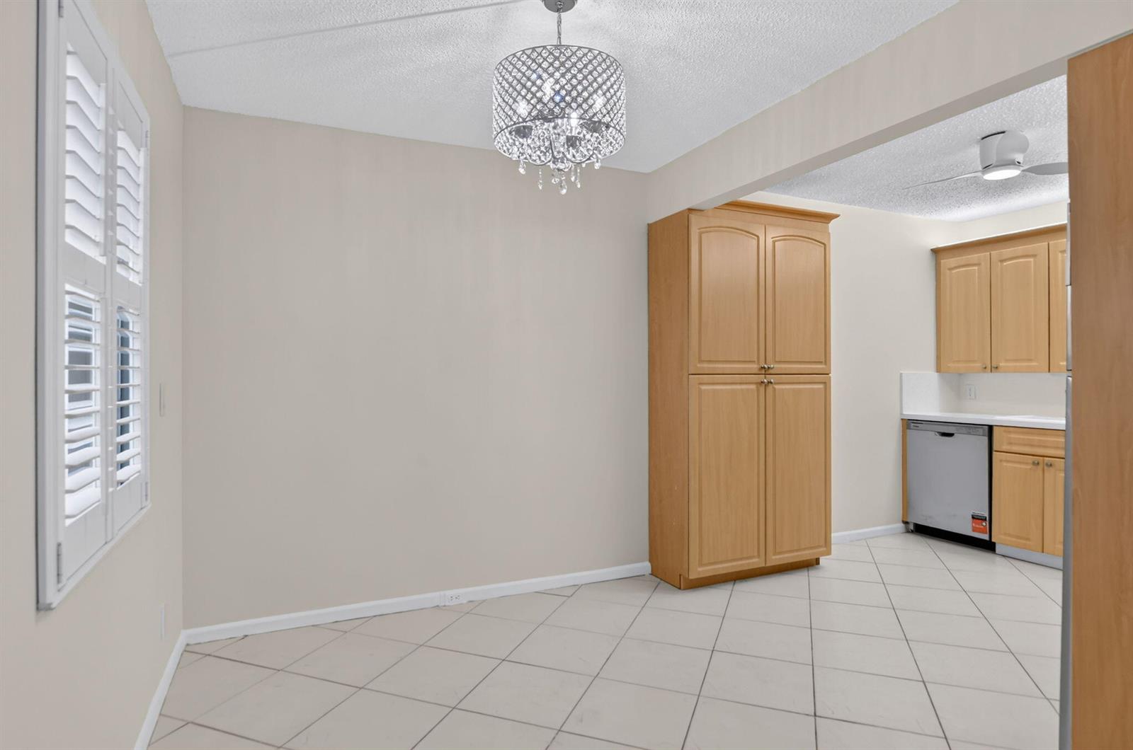 A dining area with a crystal chandelier, tile flooring, and a tall wooden pantry cabinet — 3057 Yarmouth C, Boca Raton FL 33434, BOCA RATON, FL
