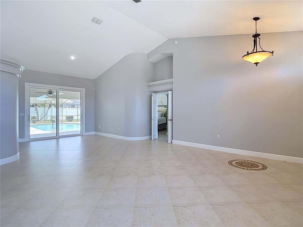 A spacious living room features light tile flooring, vaulted ceilings, and a view of a pool — 4105 ANGEL WING COURT, LUTZ, FL