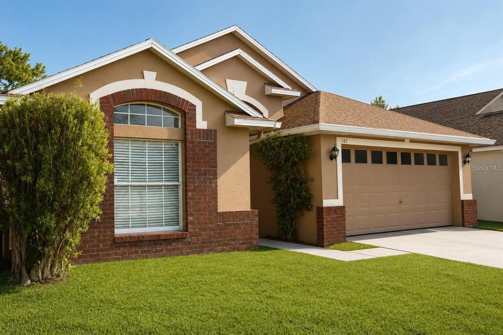 A tan stucco house with a brick-accented window, a two-car garage, and a green lawn — 145 THORNBURY DRIVE, KISSIMMEE, FL
