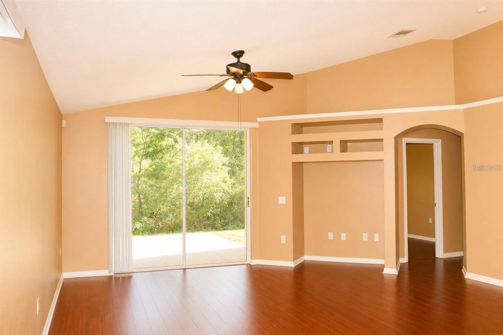 A living room with wood-look flooring, a ceiling fan, built-in shelving, and sliding glass doors — 145 THORNBURY DRIVE, KISSIMMEE, FL