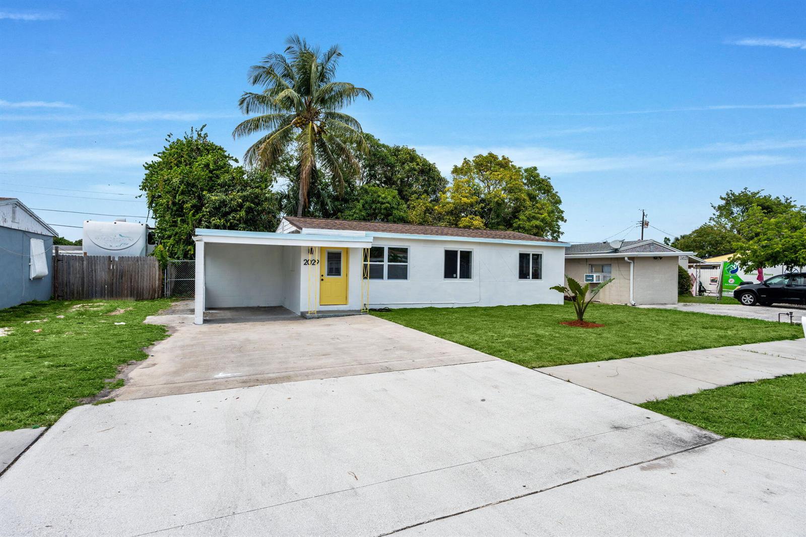 A single-story white house with a yellow front door and a concrete carport — 2029 Ardmore Road, West Palm Beach FL 33409, WEST PALM BEACH, FL