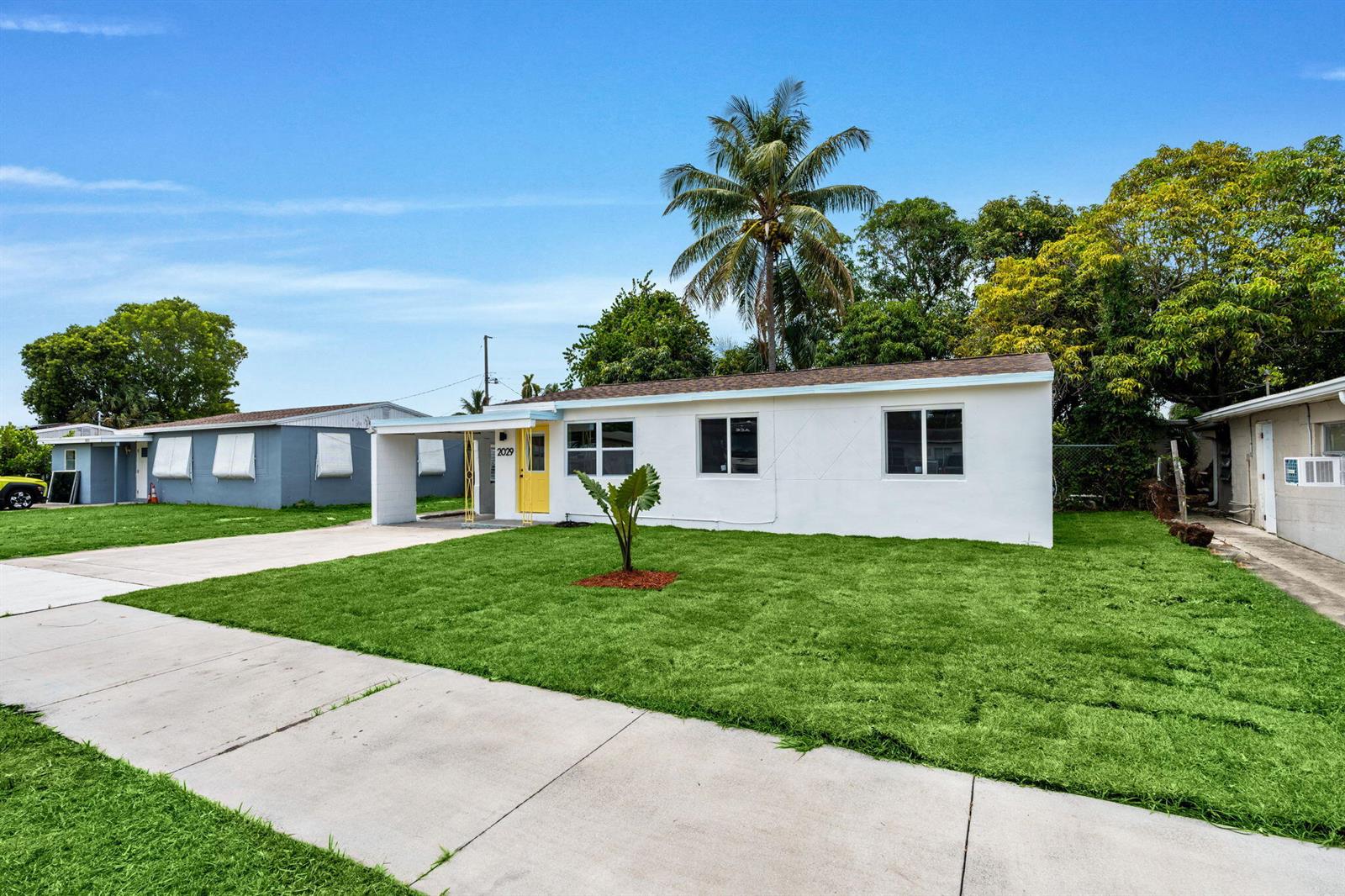 A white single-story house with a yellow front door and a palm tree in front — 2029 Ardmore Road, West Palm Beach FL 33409, WEST PALM BEACH, FL