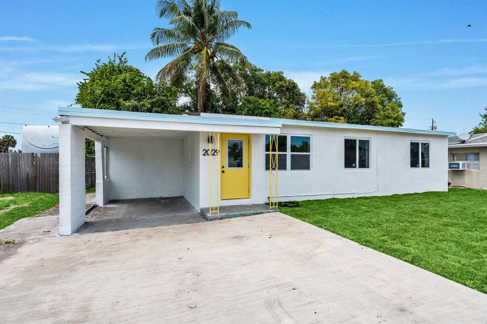 A white single-story house features a yellow front door, a carport, and a palm tree — 2029 Ardmore Road, West Palm Beach FL 33409, WEST PALM BEACH, FL