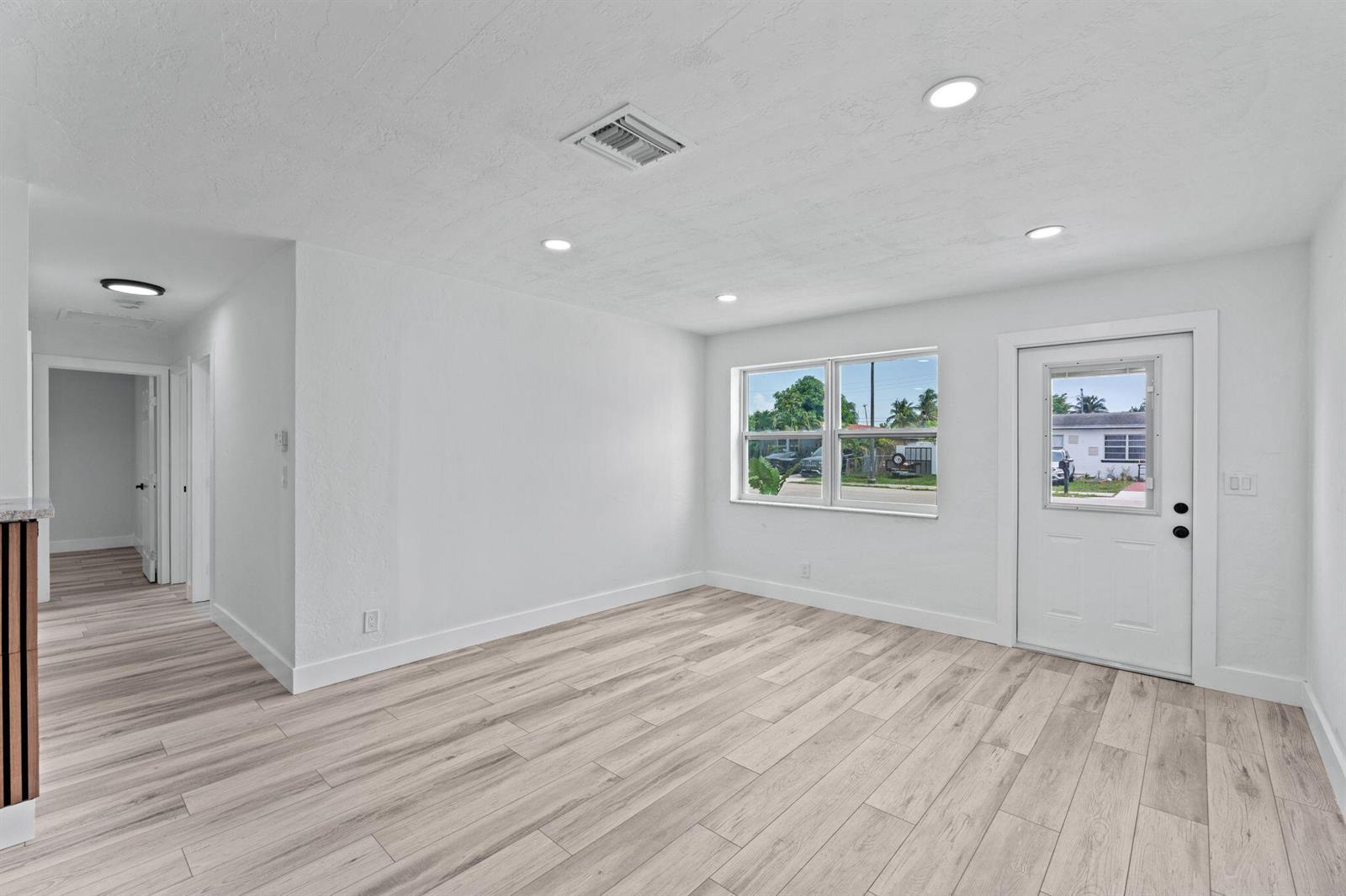 A bright, empty room with white walls, light wood-look flooring, recessed lighting, and a door — 2029 Ardmore Road, West Palm Beach FL 33409, WEST PALM BEACH, FL