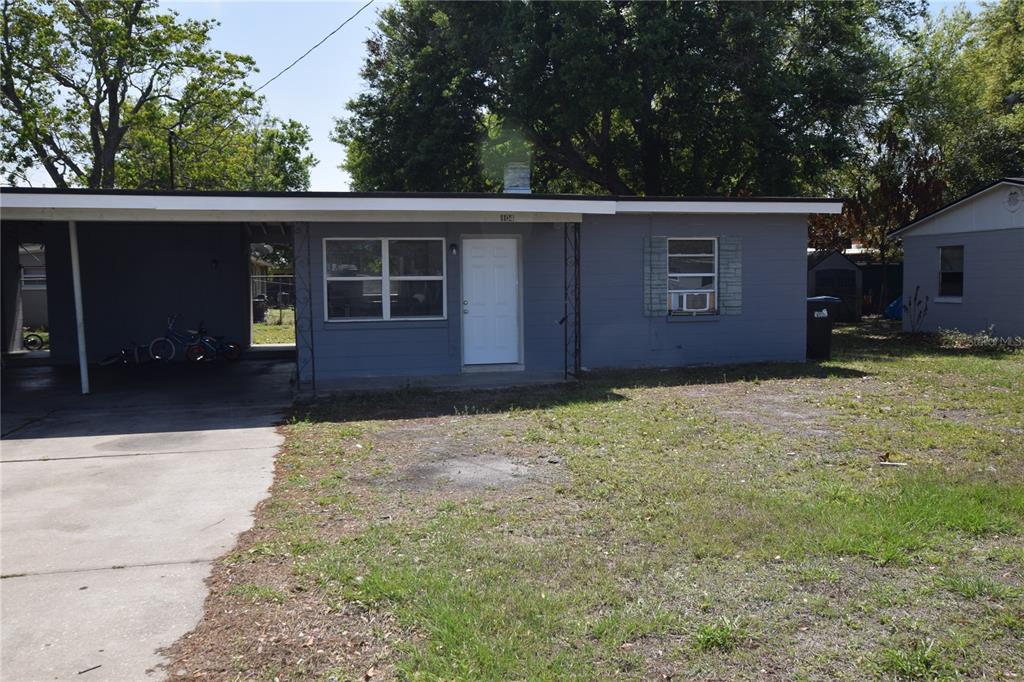A gray, single-story house features a flat roof, a carport, and a front lawn — 104 W LANCASTER ROAD, ORLANDO, FL
