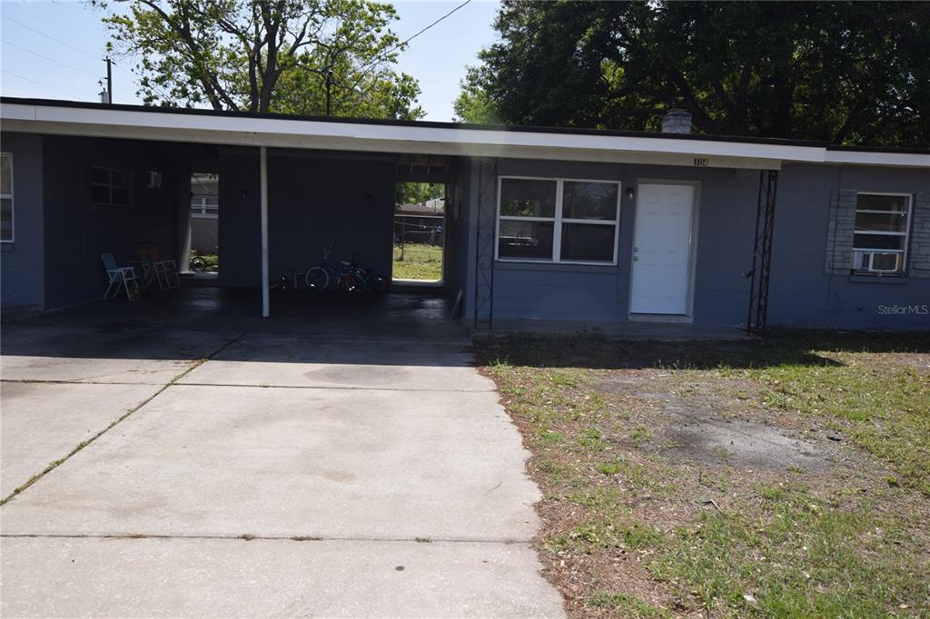 A gray house features a concrete driveway, a covered carport, and a white front door — 104 W LANCASTER ROAD, ORLANDO, FL