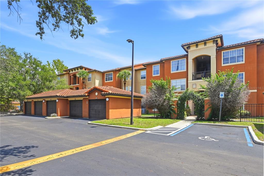 An exterior view of a multi-story apartment building with attached garages and a parking lot — 5572 METROWEST BOULEVARD UNIT 5-304, ORLANDO, FL