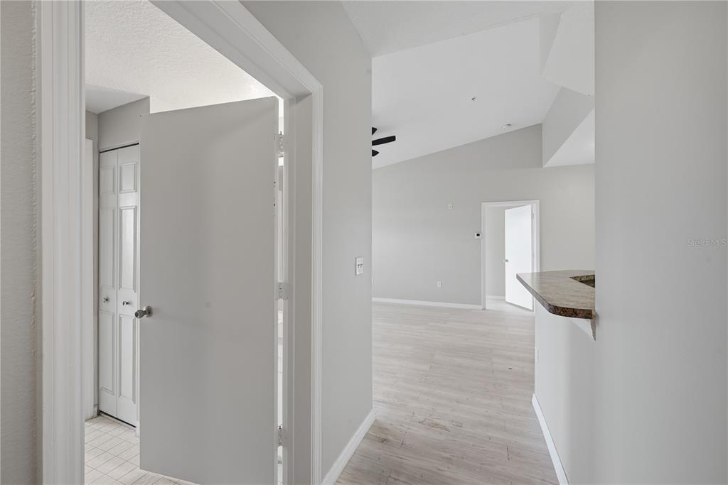 A hallway with light wood-look flooring leads to an open living area with vaulted ceilings — 5572 METROWEST BOULEVARD UNIT 5-304, ORLANDO, FL