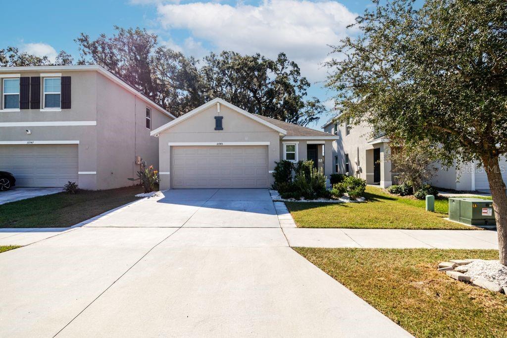 A single-story house with a beige exterior, a two-car garage, and a concrete driveway — 10945 TRAILING VINE DRIVE, TAMPA, FL