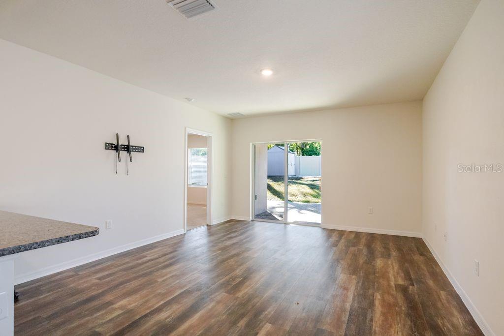 An empty living room features wood-look flooring, beige walls, and a sliding glass door — 10945 TRAILING VINE DRIVE, TAMPA, FL