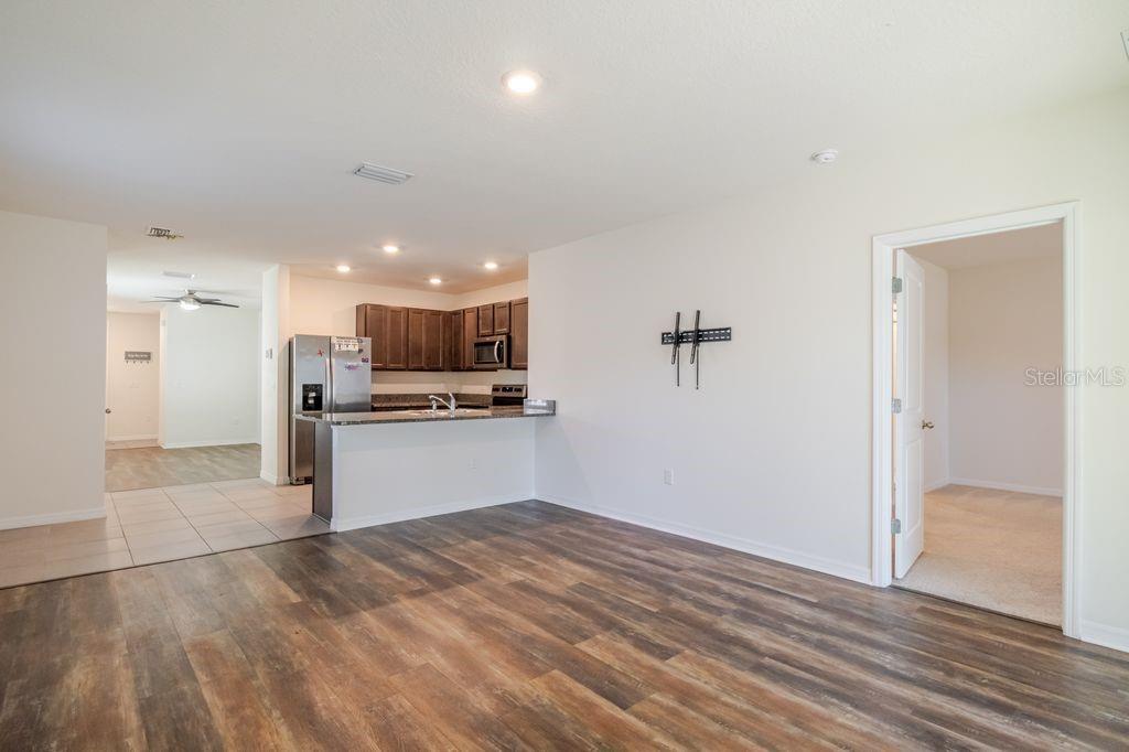 An open-concept living area features wood-look flooring, a kitchen with dark cabinets, and carpeted rooms — 10945 TRAILING VINE DRIVE, TAMPA, FL