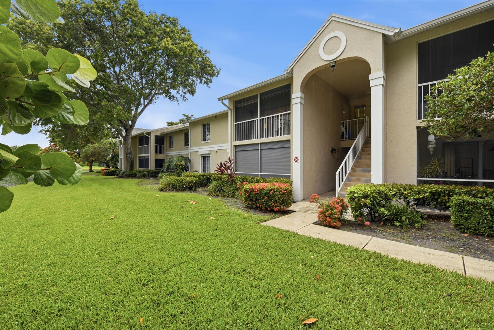 A two-story apartment building with a beige stucco exterior, screened balconies, and a grassy lawn — 13811 Oneida Drive # F2, Delray Beach FL 33446, DELRAY BEACH, FL