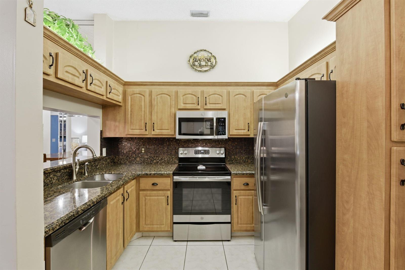 A kitchen features light wood cabinets, granite countertops, stainless steel appliances, and a tiled floor — 13811 Oneida Drive # F2, Delray Beach FL 33446, DELRAY BEACH, FL