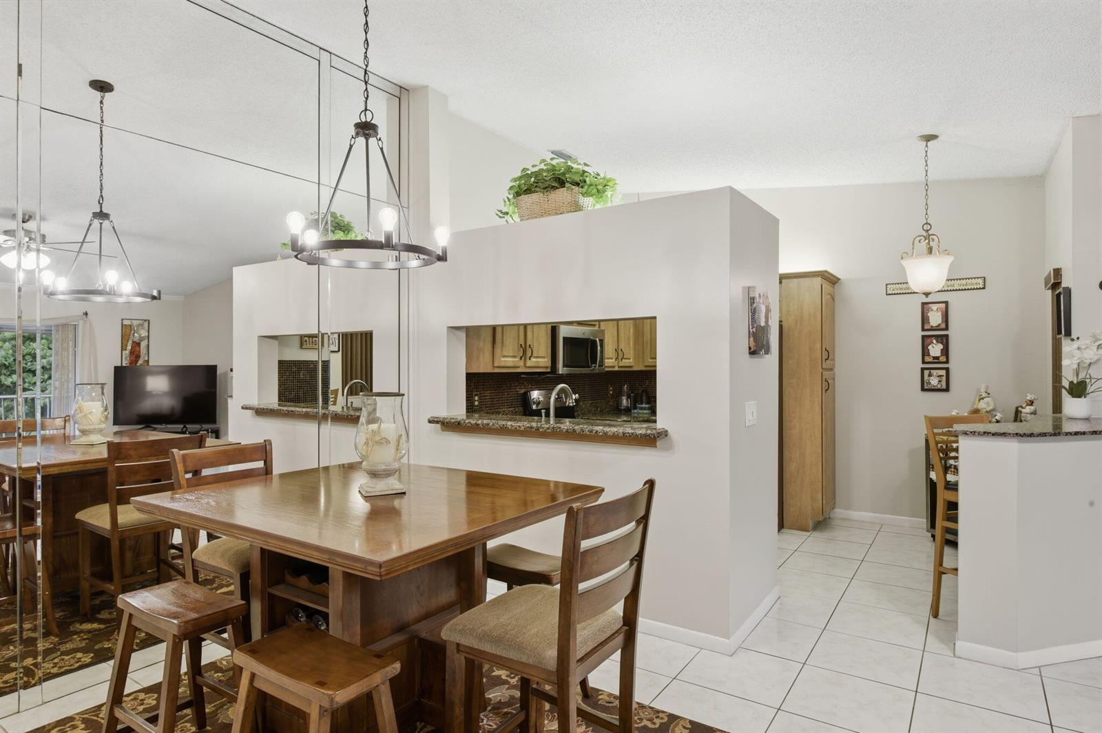 A dining area with a wooden table, mirrored wall, and a pass-through to the kitchen — 13811 Oneida Drive # F2, Delray Beach FL 33446, DELRAY BEACH, FL