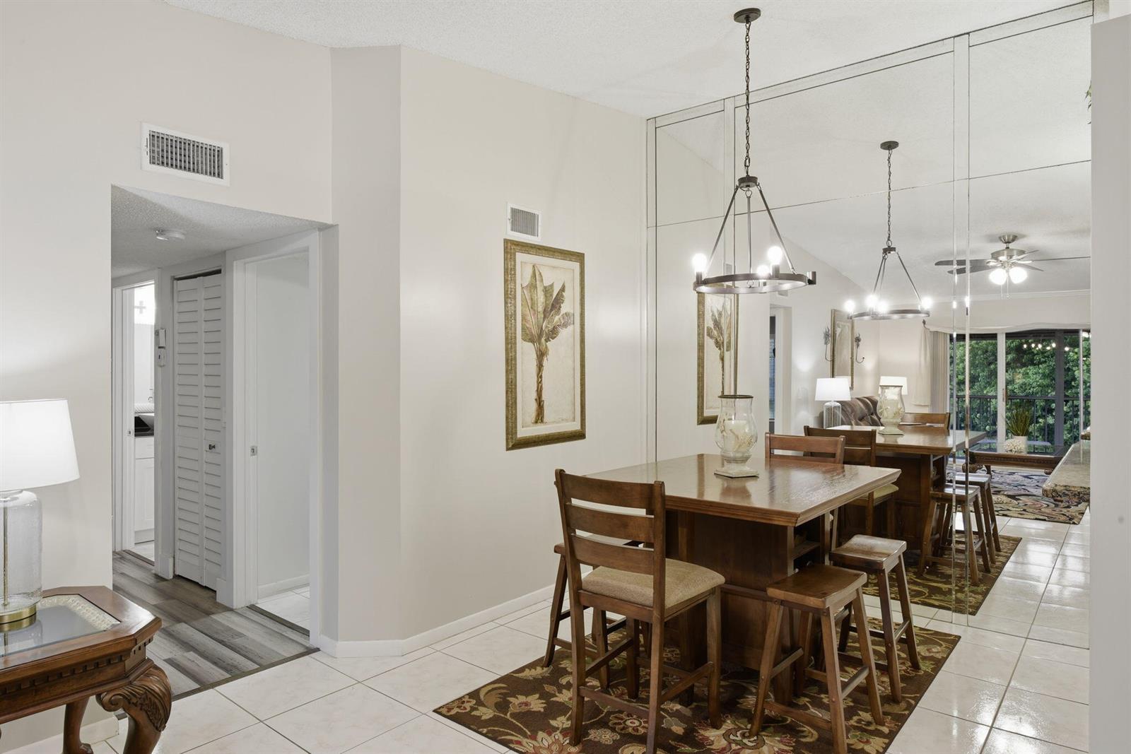 A dining area features a wooden table, chairs, a patterned rug, and a mirrored wall — 13811 Oneida Drive # F2, Delray Beach FL 33446, DELRAY BEACH, FL