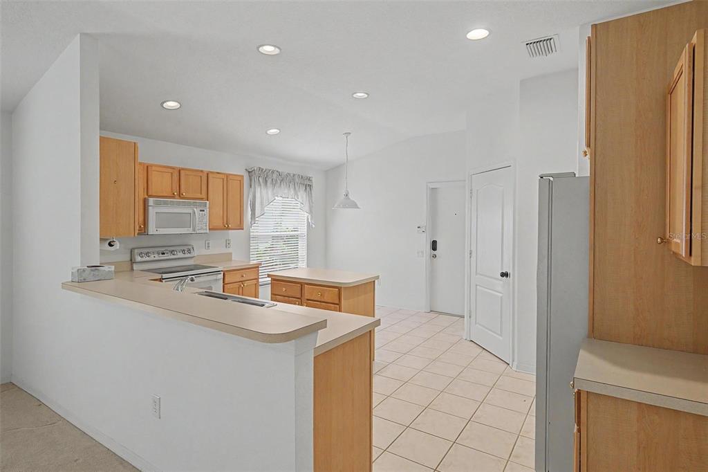 A kitchen with light wood cabinets, white appliances, and a central island on tile flooring — 5526 GALLANT FOX COURT, WESLEY CHAPEL, FL