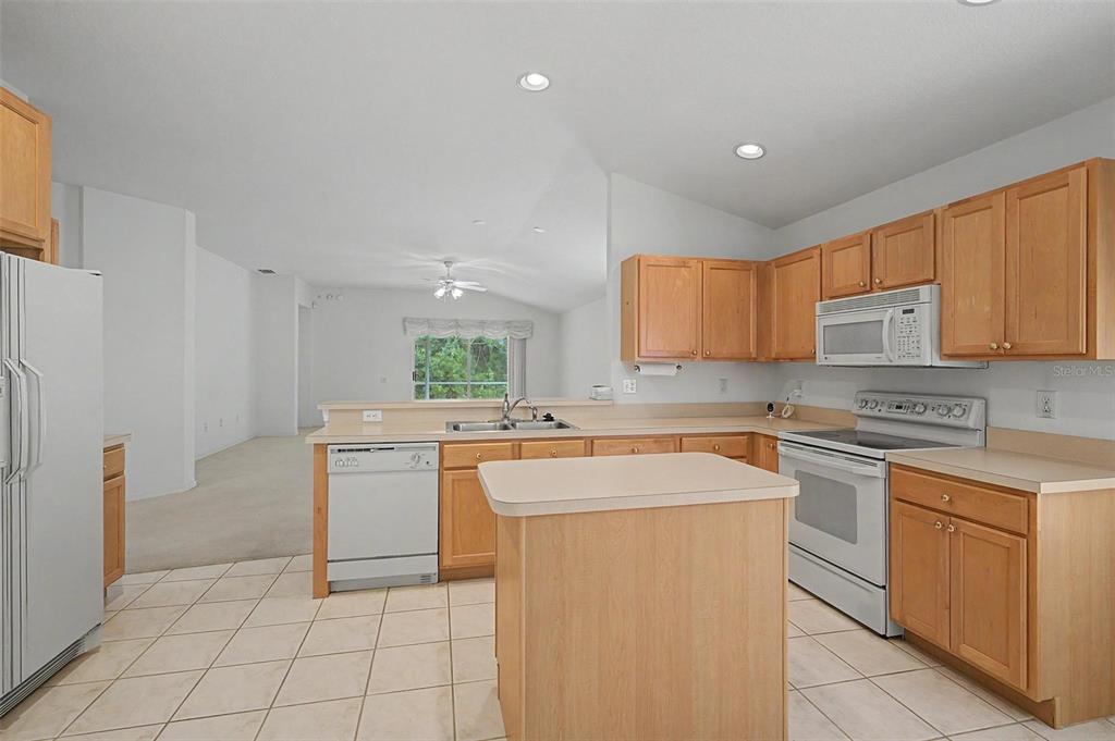 A kitchen with light wood cabinets, white appliances, a center island, and tiled flooring — 5526 GALLANT FOX COURT, WESLEY CHAPEL, FL