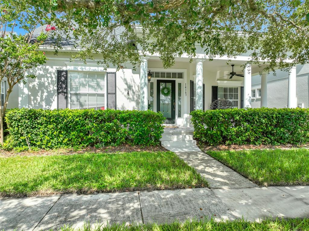 A white house with a front porch, columns, and a manicured hedge in the yard — 14163 CHICORA CROSSING BOULEVARD, ORLANDO, FL