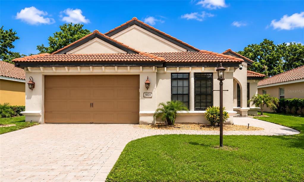 A single-story house with a tan stucco exterior, a brown garage door, and a tiled roof — 5624 AARON COURT, SARASOTA, FL