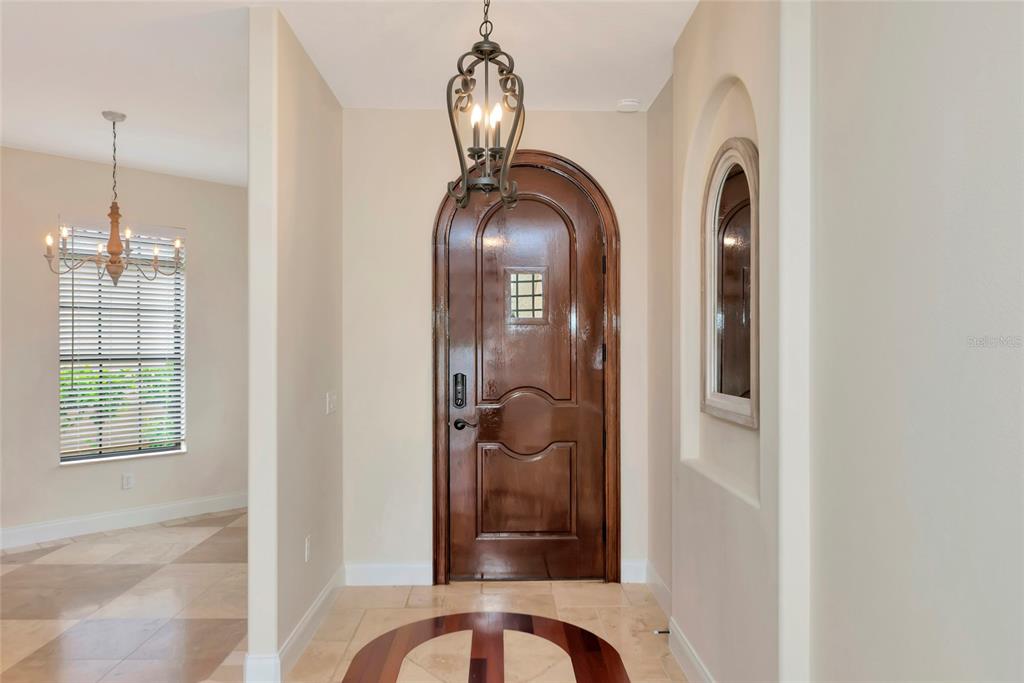An entryway features a dark arched wooden door, a hanging lantern, and beige tile flooring — 5624 AARON COURT, SARASOTA, FL
