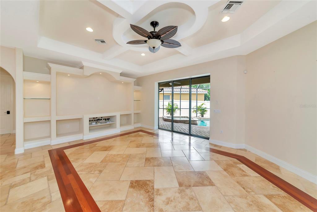 A living room features a tray ceiling, built-in shelving, tile flooring, and sliding glass doors — 5624 AARON COURT, SARASOTA, FL