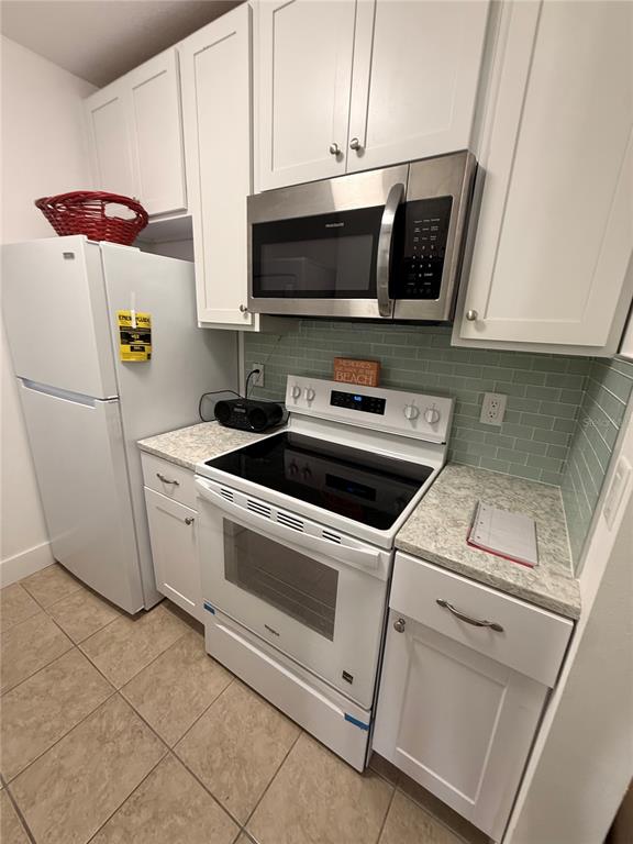A kitchen features white cabinets, stainless steel appliances, and a light green subway tile backsplash — 159 MEDALLION BOULEVARD UNIT A, MADEIRA BEACH, FL