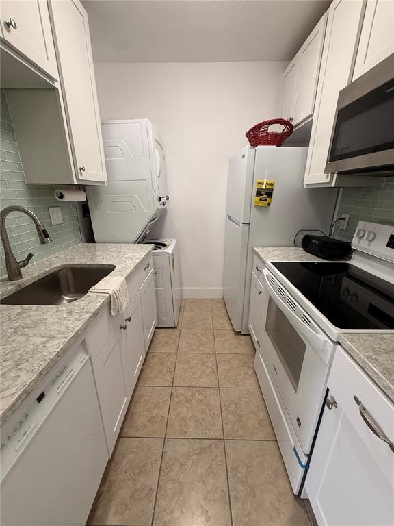 A galley kitchen features white cabinets, stainless steel appliances, a sink, and a stacked washer-dryer — 159 MEDALLION BOULEVARD UNIT A, MADEIRA BEACH, FL