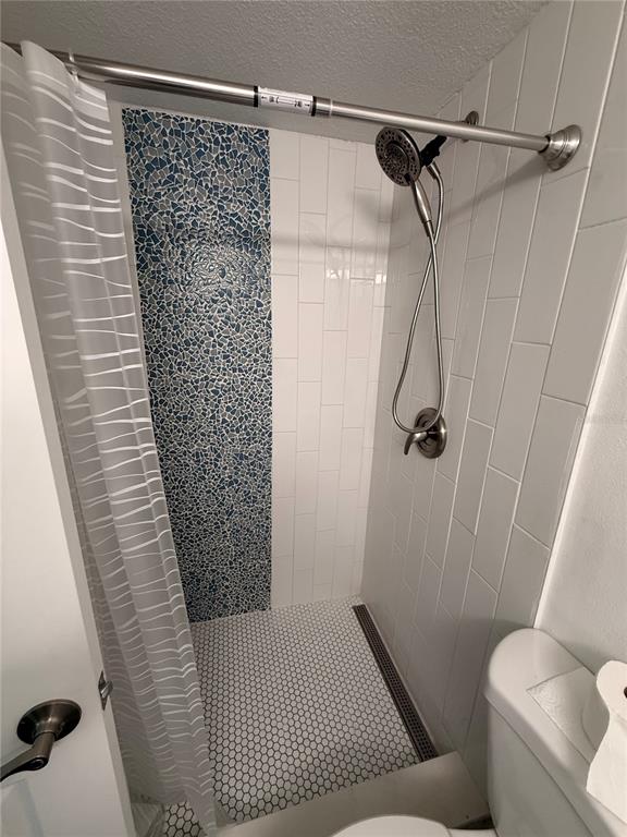 A shower stall features white subway tiles, a blue mosaic accent wall, and hexagonal floor tiles — 159 MEDALLION BOULEVARD UNIT A, MADEIRA BEACH, FL