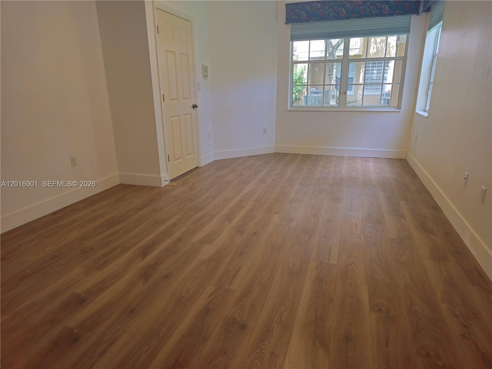 An empty room features light wood-look flooring, white walls, and a window with blinds — 14715 Balgowan Rd # 9, Miami Lakes FL 33016, MIAMI LAKES, FL