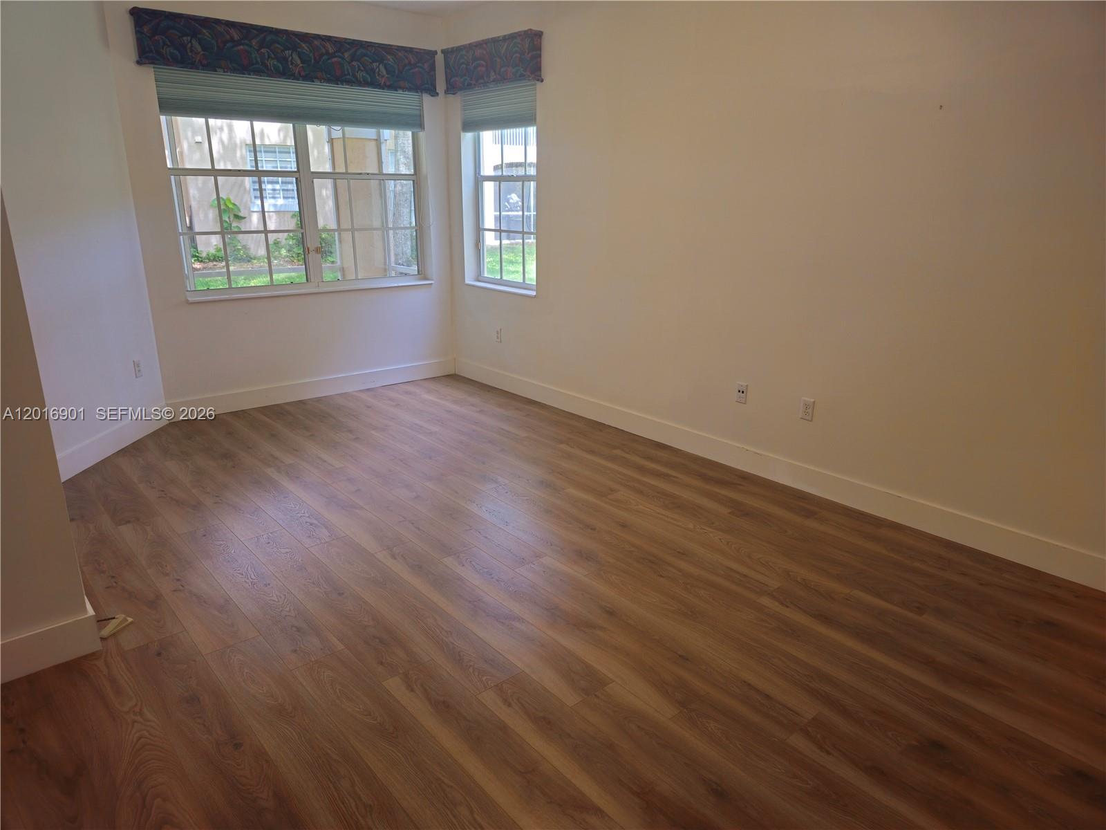 An empty room features wood-look flooring, white walls, and two windows with patterned valances — 14715 Balgowan Rd # 9, Miami Lakes FL 33016, MIAMI LAKES, FL