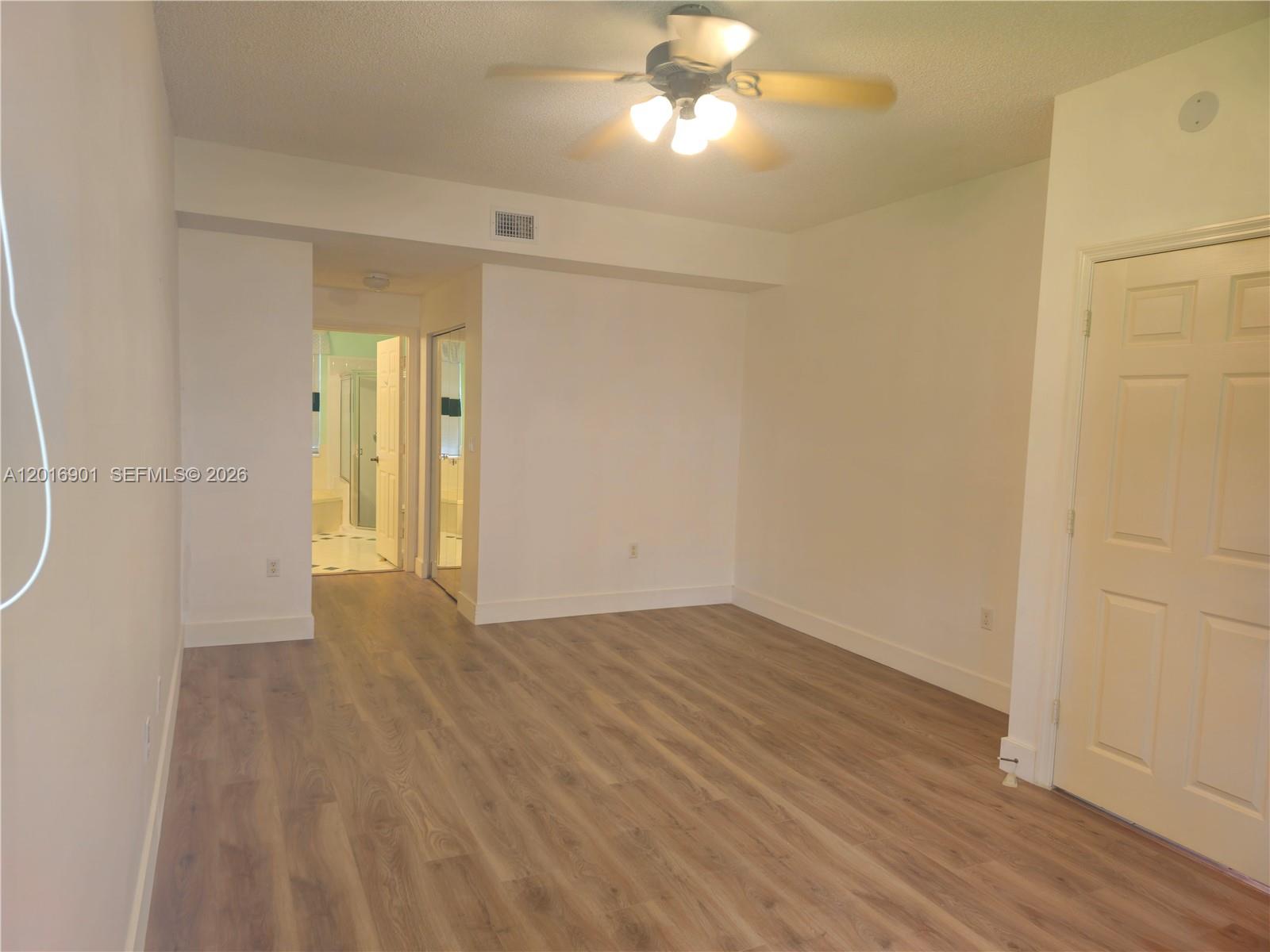 This bedroom features light wood-look flooring, white walls, a ceiling fan, and an attached bathroom — 14715 Balgowan Rd # 9, Miami Lakes FL 33016, MIAMI LAKES, FL