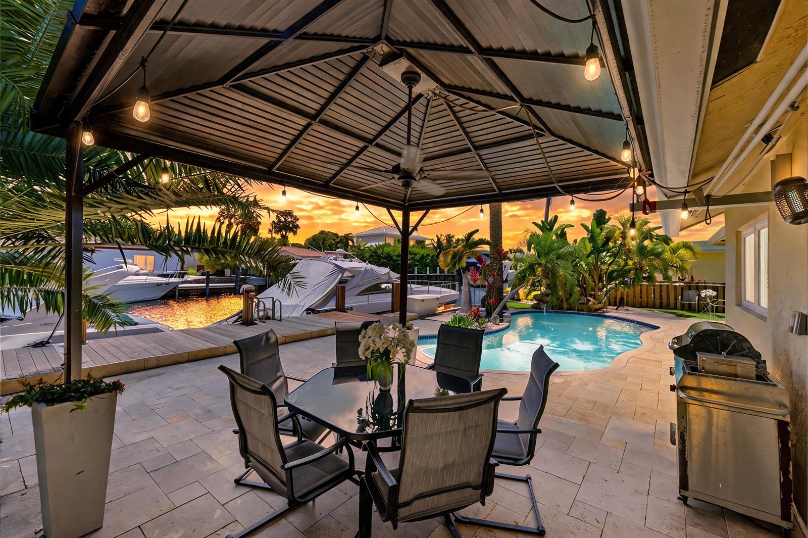 A patio with a dining set, gazebo, pool, and boat dock at sunset — 390 SE 12th Avenue, Pompano Beach FL 33060, POMPANO BEACH, FL