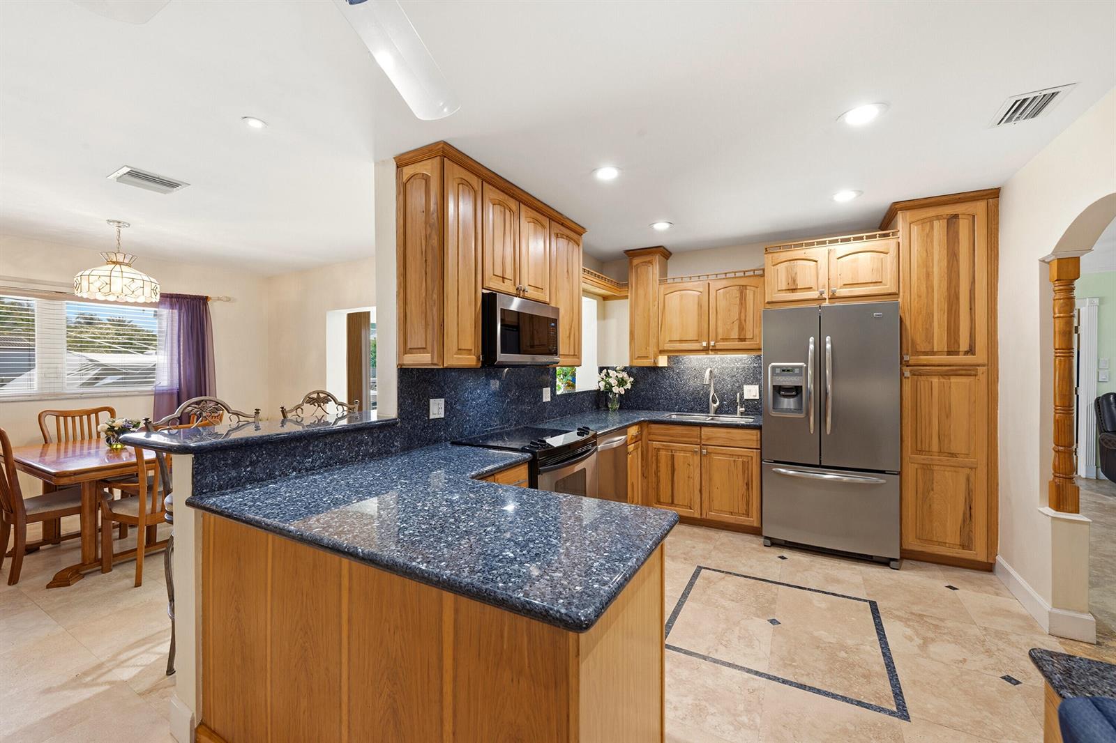 A kitchen features natural wood cabinets, blue granite countertops, and stainless steel appliances — 390 SE 12th Avenue, Pompano Beach FL 33060, POMPANO BEACH, FL