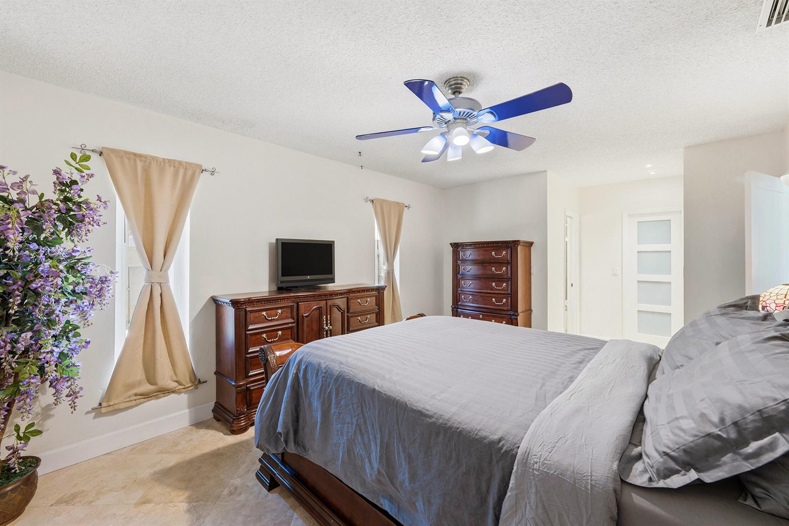 A bedroom features a bed with grey bedding, wooden furniture, and a ceiling fan — 390 SE 12th Avenue, Pompano Beach FL 33060, POMPANO BEACH, FL