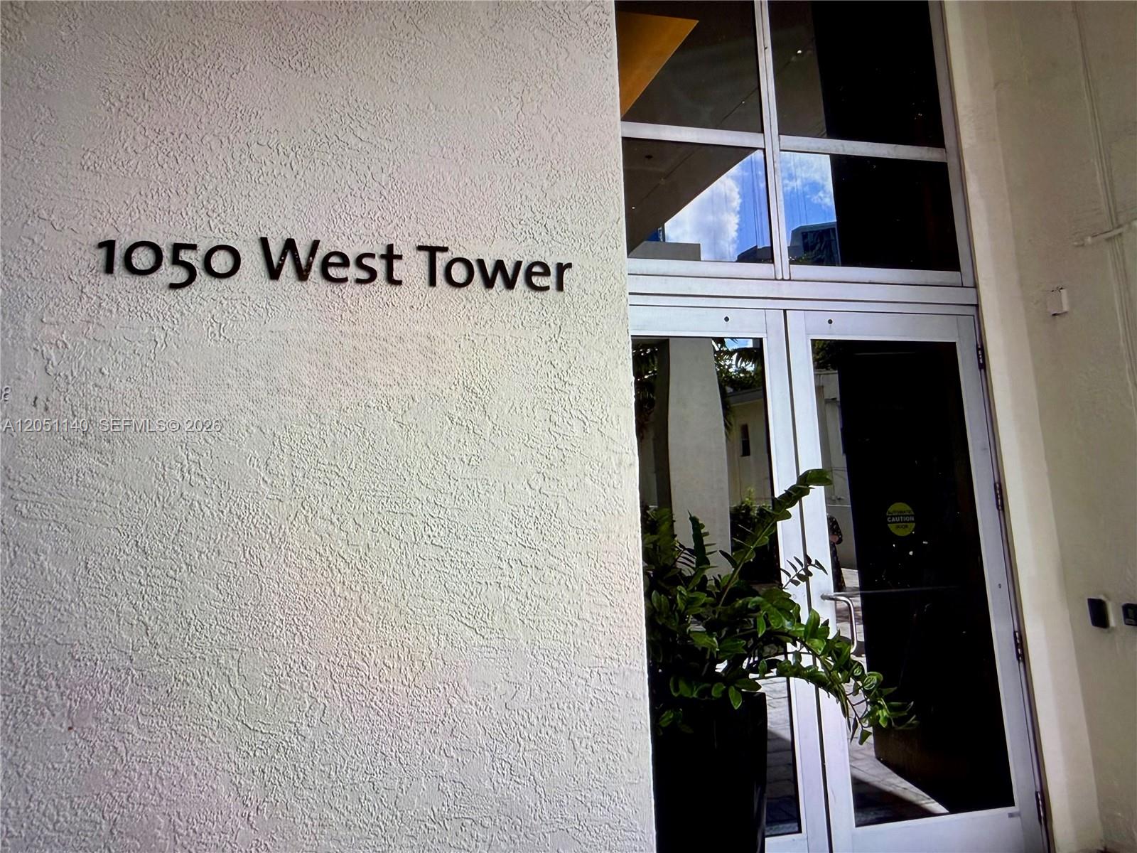 The exterior entrance of a building features a textured wall with signage and glass doors — 1050 Brickell Ave # 2018, Miami FL 33131, MIAMI, FL