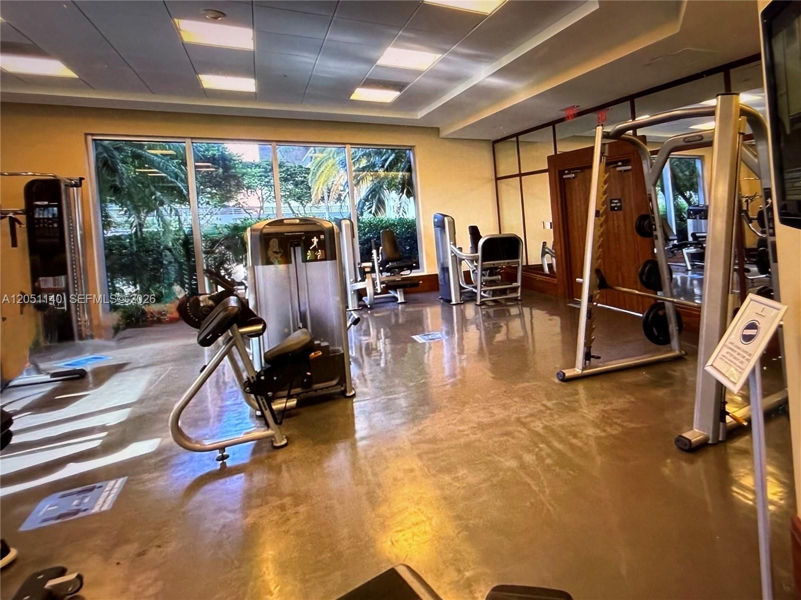 A gym features various exercise machines, large windows, and a reflective floor — 1050 Brickell Ave # 2018, Miami FL 33131, MIAMI, FL