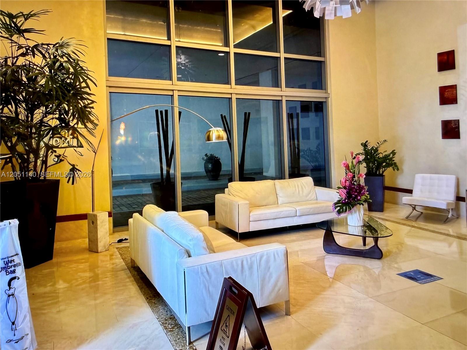 A modern lobby features white leather sofas, a glass coffee table, and large floor-to-ceiling windows — 1050 Brickell Ave # 2018, Miami FL 33131, MIAMI, FL